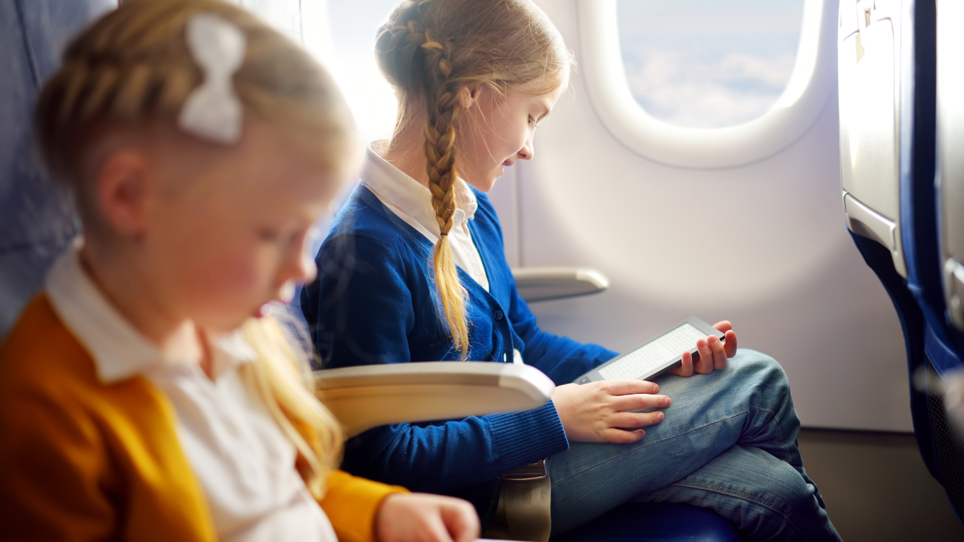 two young girls on a plane with digital devices